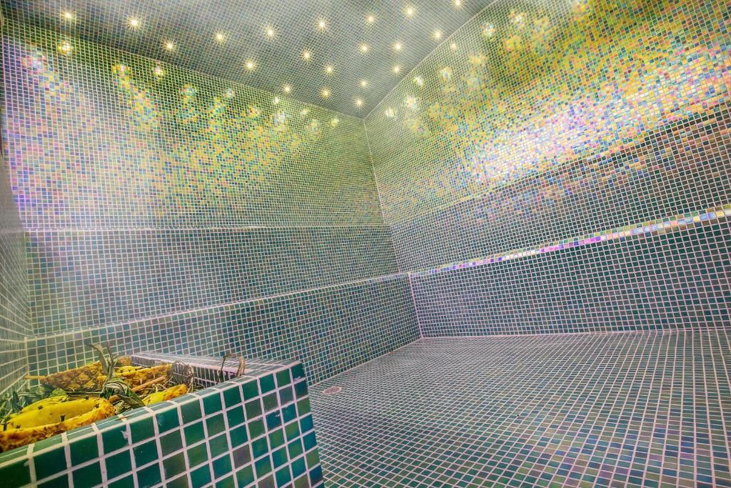 A room with a mosaic tile wall and a bathtub with a green and white tile pattern.