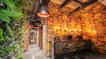A bar area with a wall covered in posters, a counter with stools, and a ceiling with exposed pipes.