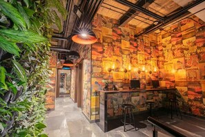A bar area with a wall covered in posters, a counter with stools, and a ceiling with exposed pipes. - Hotel V1501 Sas (San Juan de Pasto)
