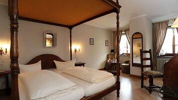 Ein traditionelles Himmelbett mit Baldachin, ein hölzerner Nachttisch, ein Sessel und ein Schreibtisch mit Lampe.