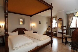 Een traditioneel ledikham met hemelbed, een houten nachtkastje, een stoel en een bureau met lamp.