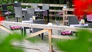 Ein Essbereich im Freien mit Holztischen und -stühlen, umgeben von Pflanzen.