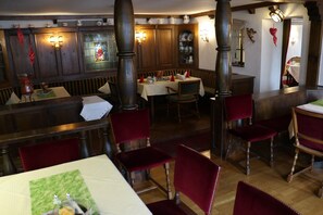 Een restaurant met houten lambrisering, rode fluweelstoelen en een glas-in-loodraam.