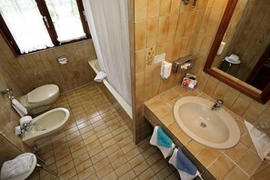 Une salle de bain avec deux toilettes, un lavabo, une baignoire et une douche.