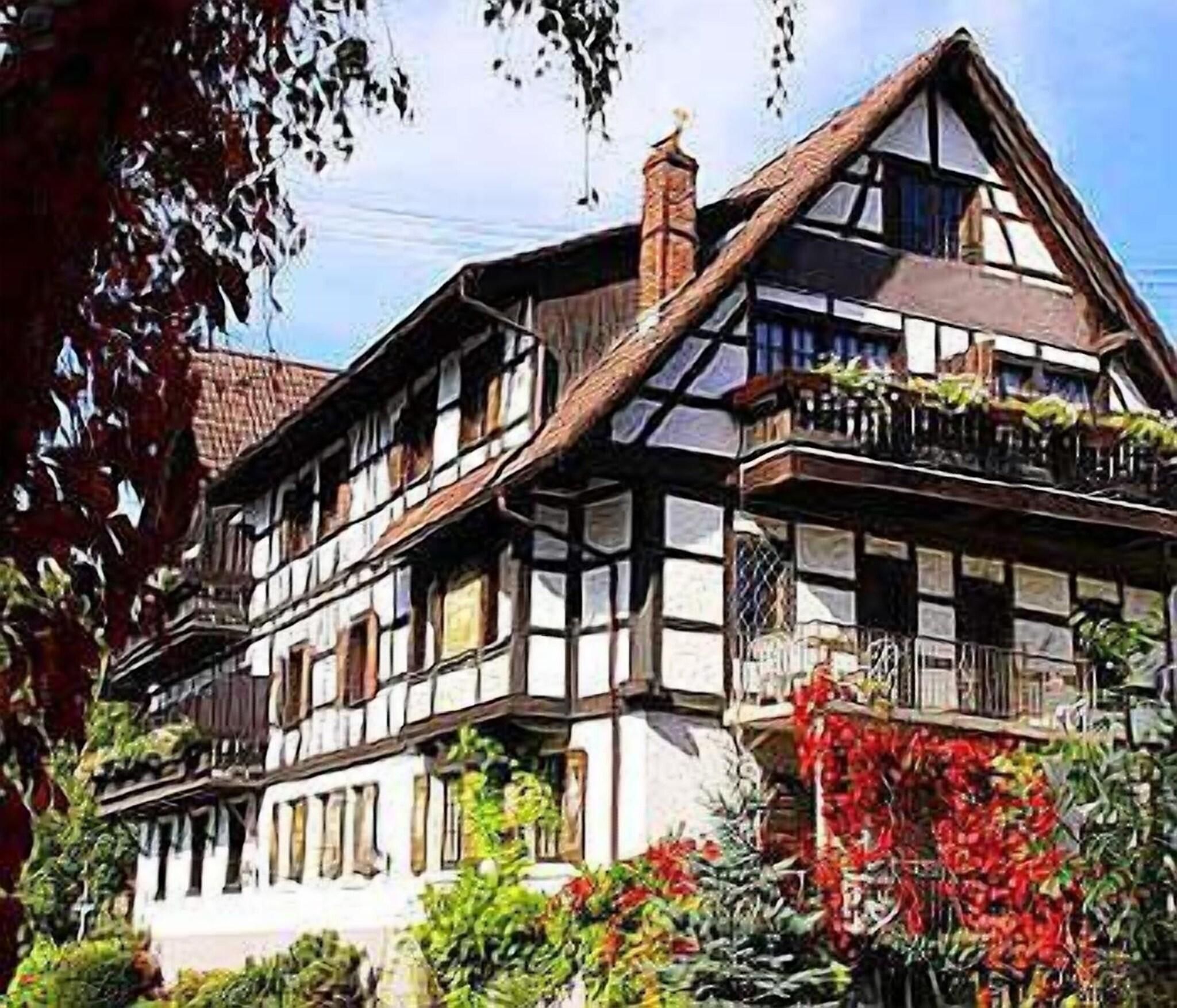 Ein traditionelles Fachwerkhäuschen mit mehreren Stockwerken, großen Fenstern und einem Balkon mit Pflanzen.