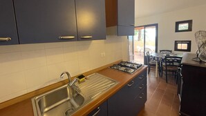 A kitchen with dark cabinets, a stainless steel sink, and a gas stove. - Collina sul Golfo 13 (Porto Azzurro)