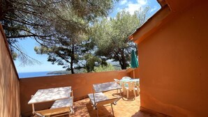 A terrace with a table and chairs, overlooking a body of water and trees. - Collina sul Golfo 13 (Porto Azzurro)