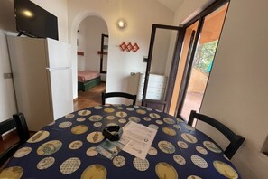 Un coin repas avec une table dressée pour deux personnes, un réfrigérateur et un lit en arrière-plan.