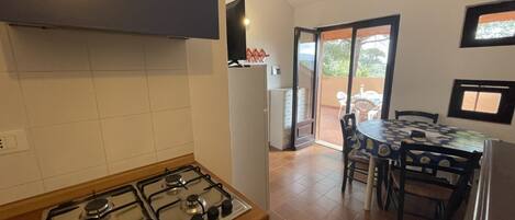 A kitchen with a gas stove, a refrigerator, and a dining area with a table and chairs.