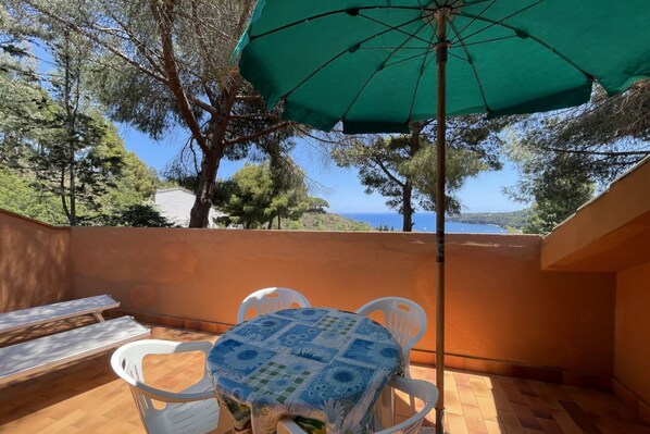 Un balcon avec une table et des chaises, un parasol vert et une vue sur la mer.