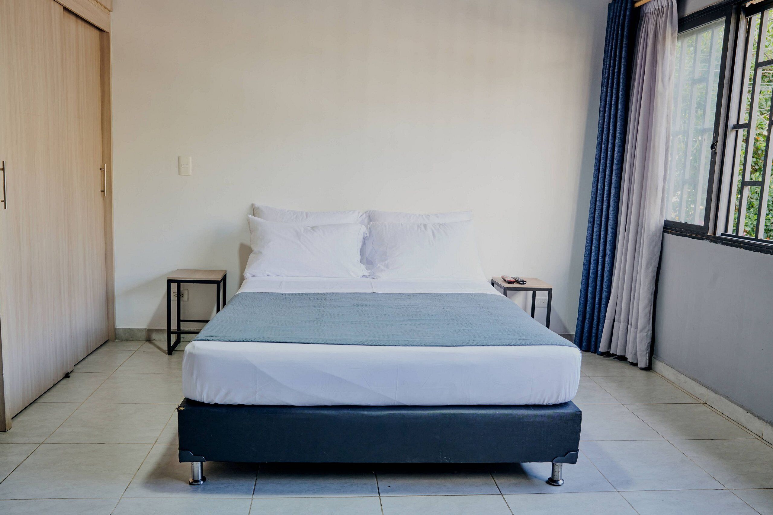 A bedroom with a bed, a bedside table, a wardrobe, and a window with curtains.