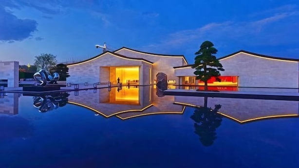Un edificio moderno con una piscina reflectante, un árbol y un cielo despejado.