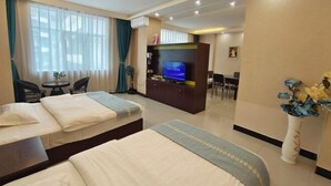 Habitación de hotel con dos camas, televisión, zona de comedor y un jarrón con flores.