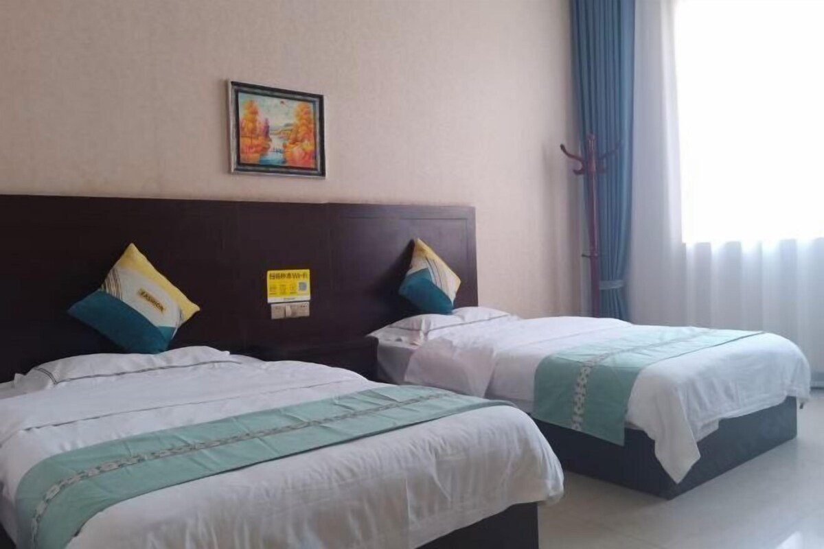 A hotel room with two beds, a headboard, a framed picture, and a window with curtains.