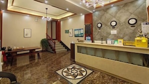 Zona de recepción de un hotel con suelo de mármol, mostrador de recepción, una escalera y un candelabro.