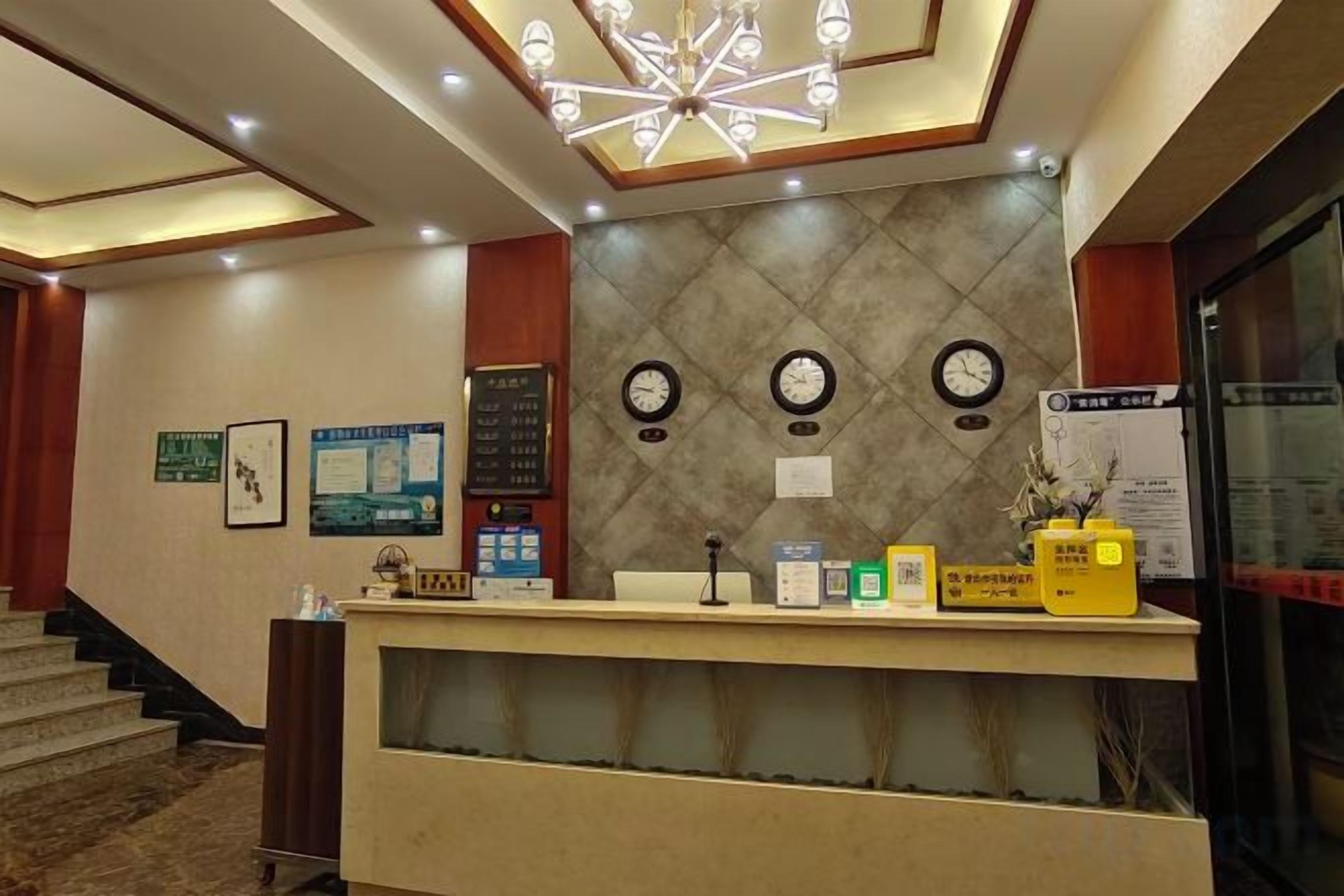 A hotel reception desk with a clock, a bulletin board, and a staircase leading to the upper floor.