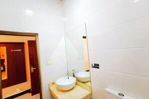 A bathroom with white tiles, a sink, a mirror, and a door. - Hurui Hotel (Mile)