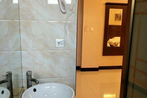 A bathroom with a white sink, two faucets, a mirror, and a shower with a hose. - Hurui Hotel (Mile)