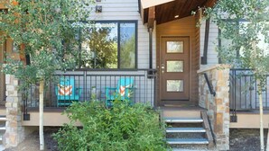 A modern house with a stone facade, a front porch with a bench, and a small garden area.