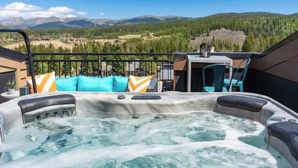 A hot tub with a mountain view, a table with chairs, and a railing.