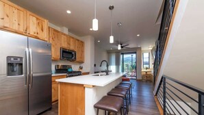 A modern kitchen with wooden cabinets, stainless steel appliances, a central island with bar stools, and a view to the outdoors.