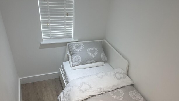 Een kleine eenpersoonskamer met een raam, witte wanden en een houten vloer.