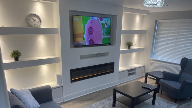 A modern living room with a flat-screen TV, grey sofa, coffee table, and built-in fireplace. - 3Br-Free Parking- Near Transport Links (London)