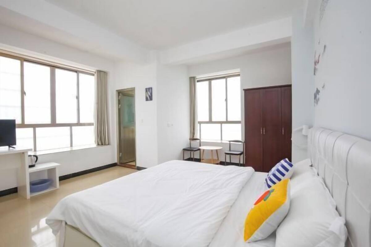 A hotel room with a large bed, a desk with a chair, a small table with two chairs, and a wardrobe.