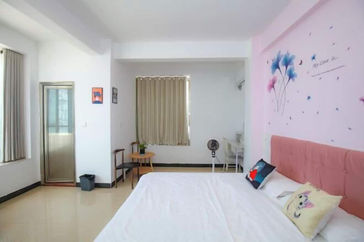 A bedroom with a bed, a desk, a chair, a window with curtains, and a wall with a floral decoration.