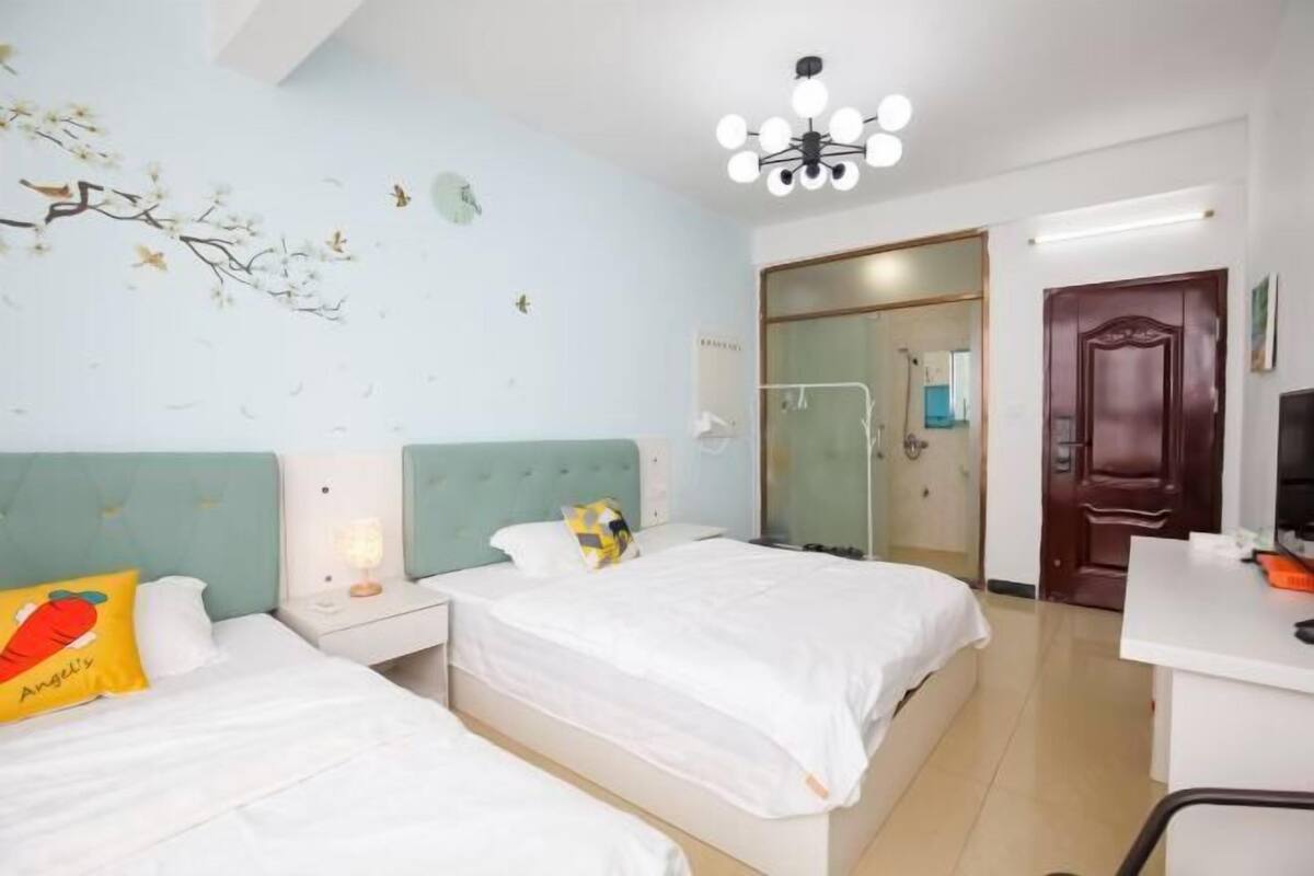 A hotel room with two beds, a desk, a mirror, and a chandelier.