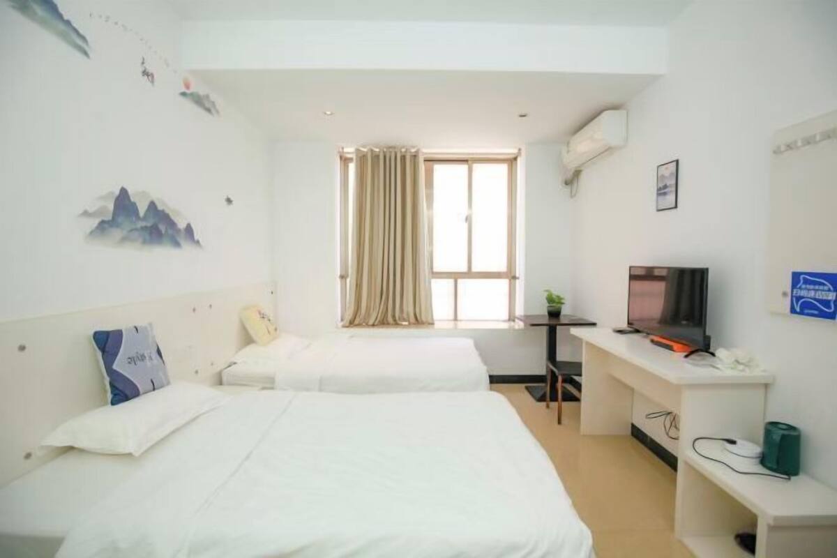 A hotel room with two beds, a desk with a television, a window with curtains, and wall decorations.