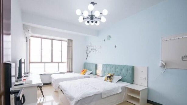 A hotel room with two beds, a desk with a computer, a chair, a window, and a ceiling light fixture. - Beihai Jiuyu Inn (Silver Beach) (Beihai)