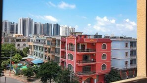 A multi-story building with balconies and a red facade, surrounded by other buildings and greenery. - Beihai Jiuyu Inn (Silver Beach) (Beihai)