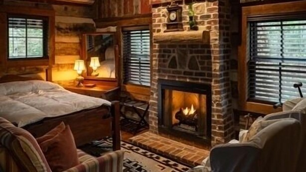 Interior acollidor d'una cabana amb sostre de fusta, una llar de pedra, un llit i una zona de seients.