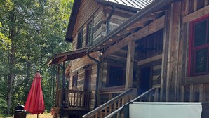 Una cabana de fusta amb una banyera d'hidromassatge a davant, un para-sol vermell i una escala que condueix al porxo.
