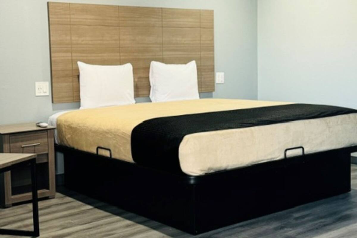 Una habitación de hotel moderna con una cama grande, un cabecero de madera, una mesita de noche y una mesilla.