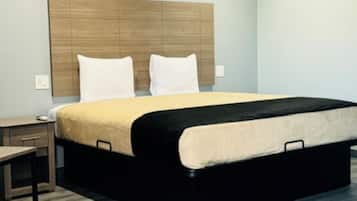 Une chambre d’hôtel moderne avec un grand lit, une tête de lit en bois, une table de chevet et une petite table de nuit.