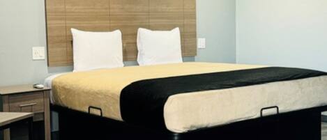 A modern hotel room with a large bed, a wooden headboard, a bedside table, and a nightstand.