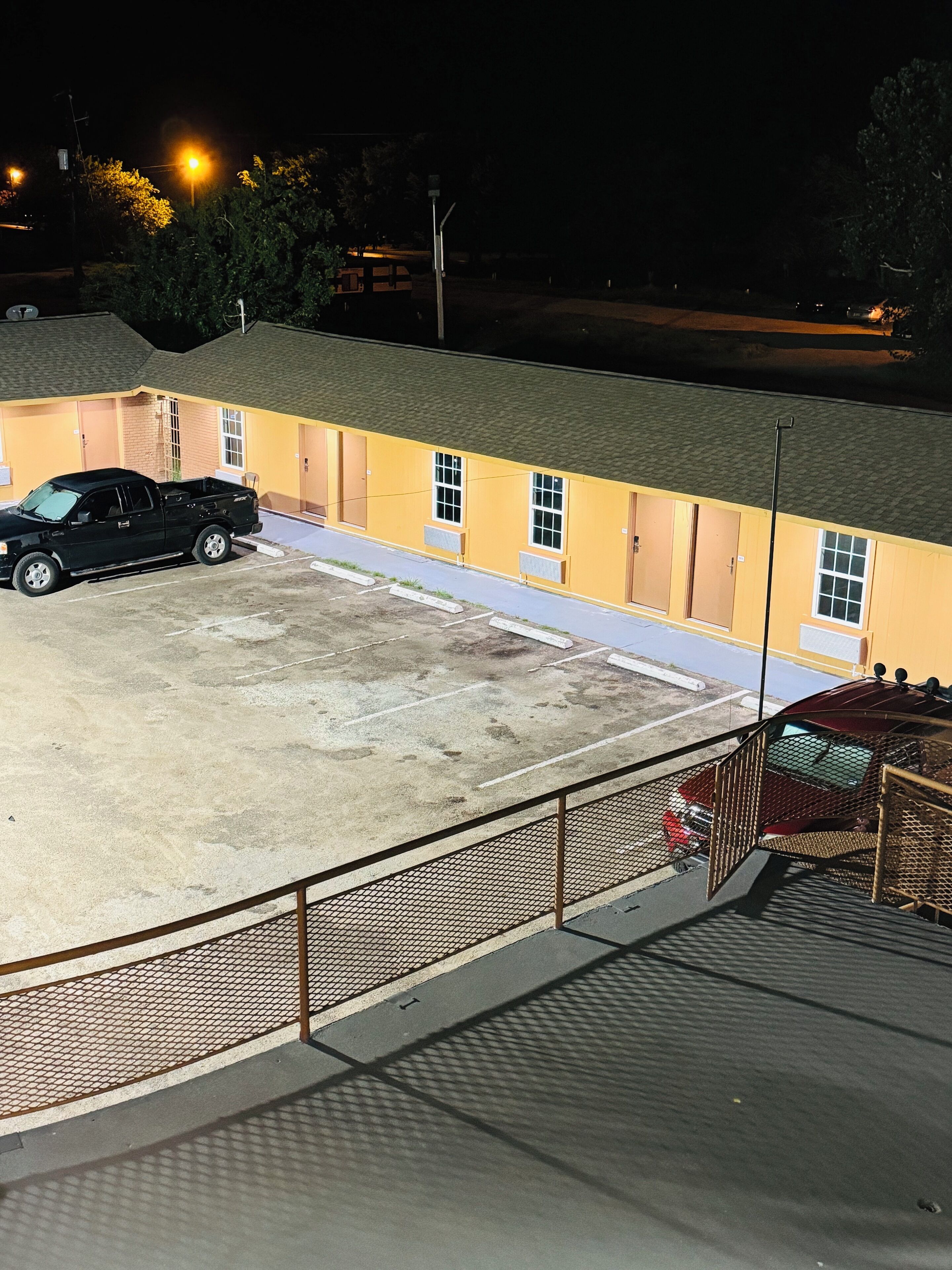 Un edificio con un estacionamiento, una camioneta negra y un coche rojo aparcados allí.