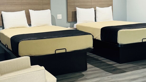 A hotel room with two beds, a sofa, and a wooden headboard. - EXPRESS INN & SUITES (El Campo)