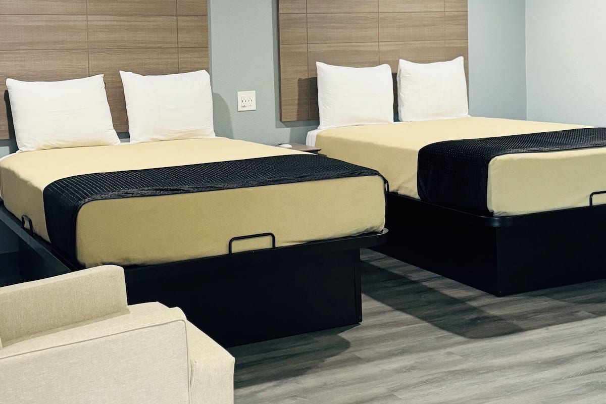 Habitación de hotel con dos camas, un sofá y un cabecero de madera.
