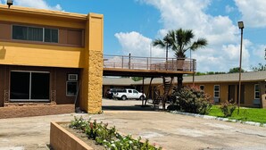 A building with a yellow facade, a covered walkway, and a parking area with a white vehicle. - EXPRESS INN & SUITES (El Campo)