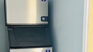 A compact, stainless steel refrigerator with a digital control panel, located in a corner of a room with light blue walls and tiled flooring. - EXPRESS INN & SUITES (El Campo)
