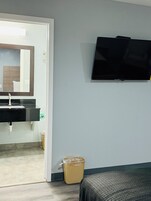 Una habitación de hotel con baño, televisor montado en la pared y un cubo de basura.