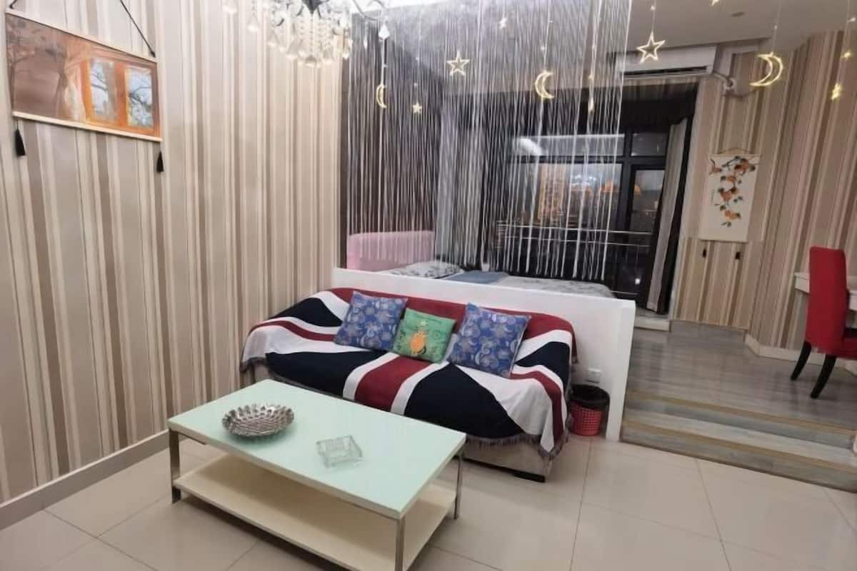 A cozy room with a striped wall, a sofa with colorful cushions, a small table, and a window with curtains.