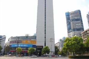 A tall building with a modern design, surrounded by other high-rise buildings and a street with trees.