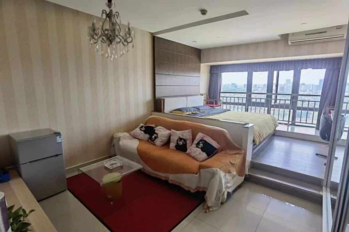 A modern hotel room with a bed, a sofa, a small desk, and a balcony with a city view.