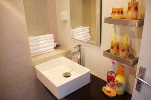 Un baño con un lavamanos blanco, un espejo y repisas con artículos de aseo.