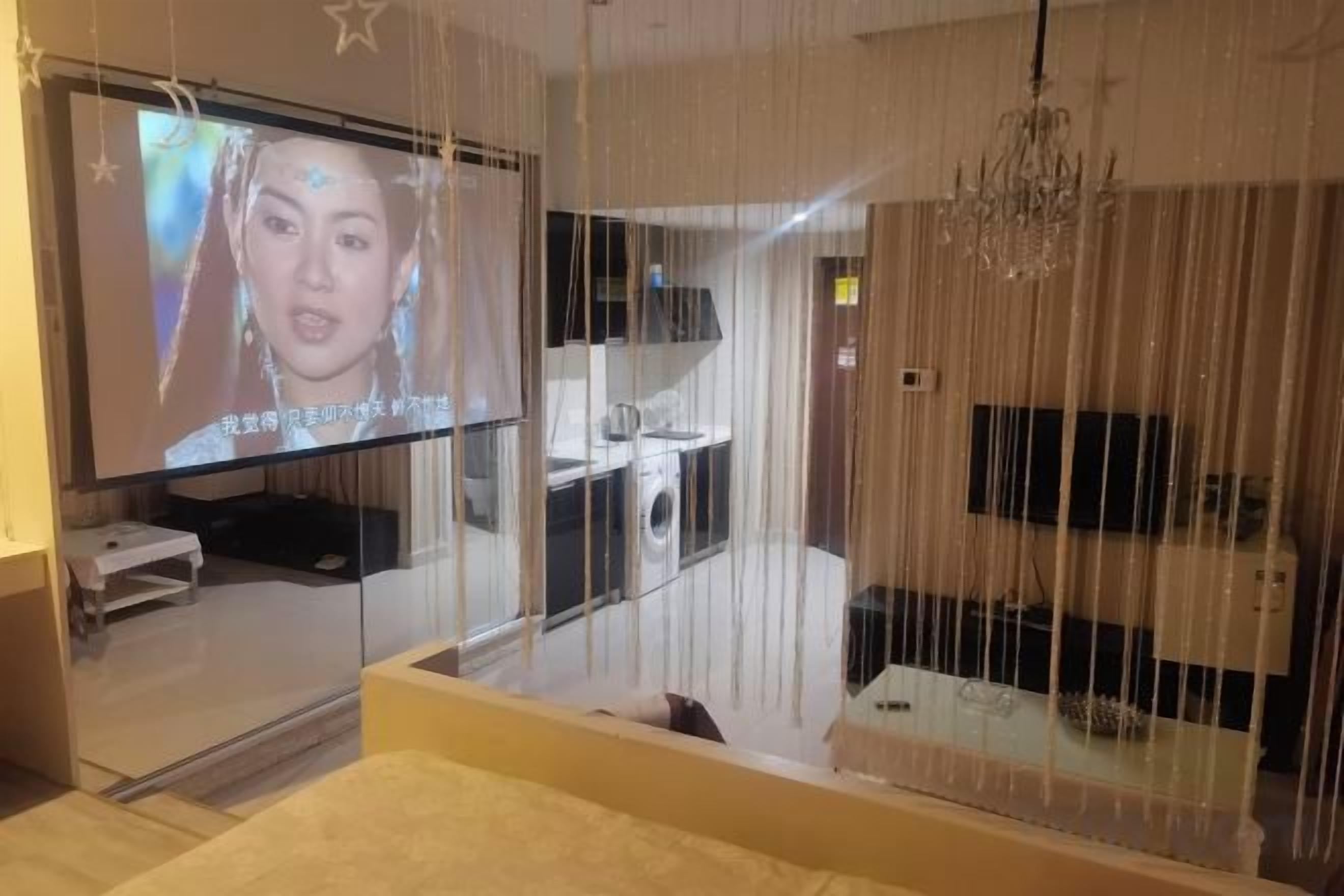 A hotel room with a large TV, a bed, and a view of the bathroom.