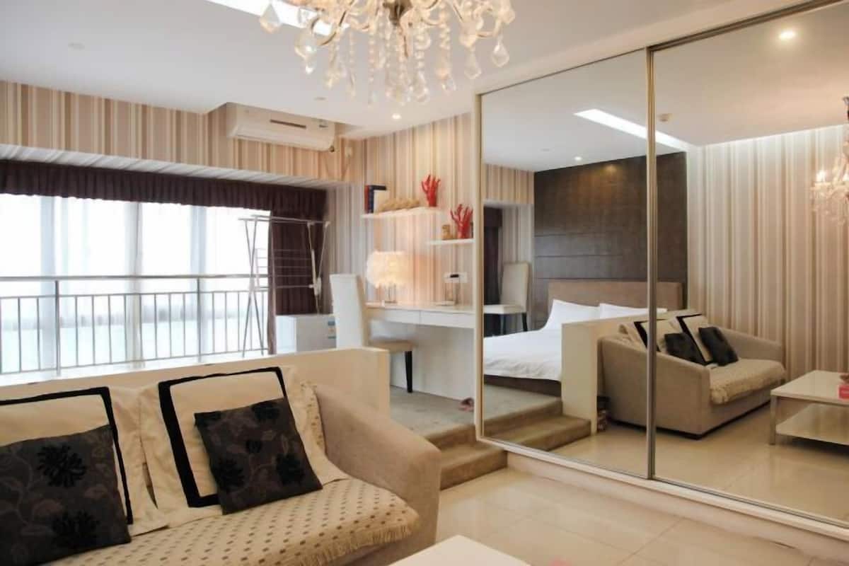 A modern hotel room with a large mirror, a sofa, a bed, and a desk.
